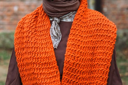 Close-up of a stylish orange knit scarf and brown outfit, perfect for fall fashion enthusiasts.