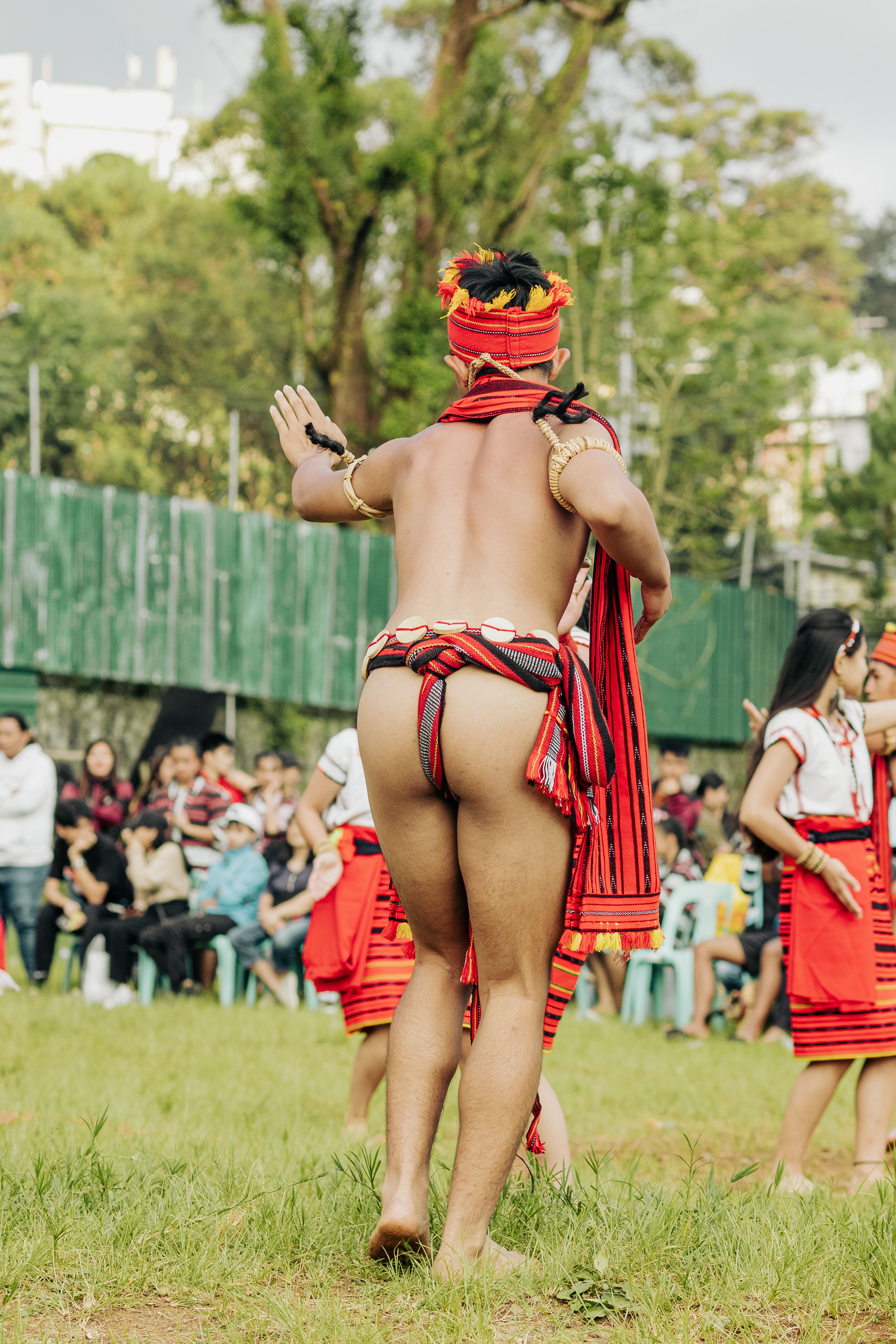 Back view of a man in traditional tribal clothing during an outdoor cultural dance event.