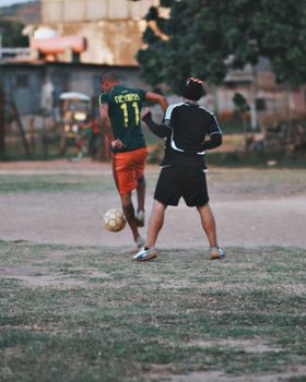 Two men playing football on a gritty town field, showing dynamic action.