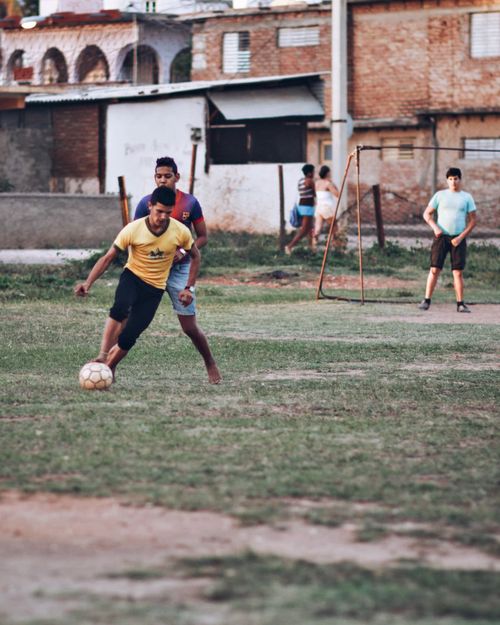 Free Teenage boys playing soccer in a city field under clear skies. Stock Photo
