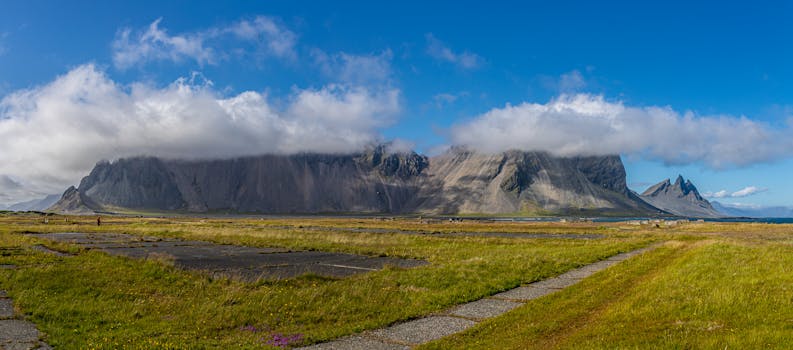 Panoramic view of majestic mountains with clouds and lush grassland, ideal for travel imagery.