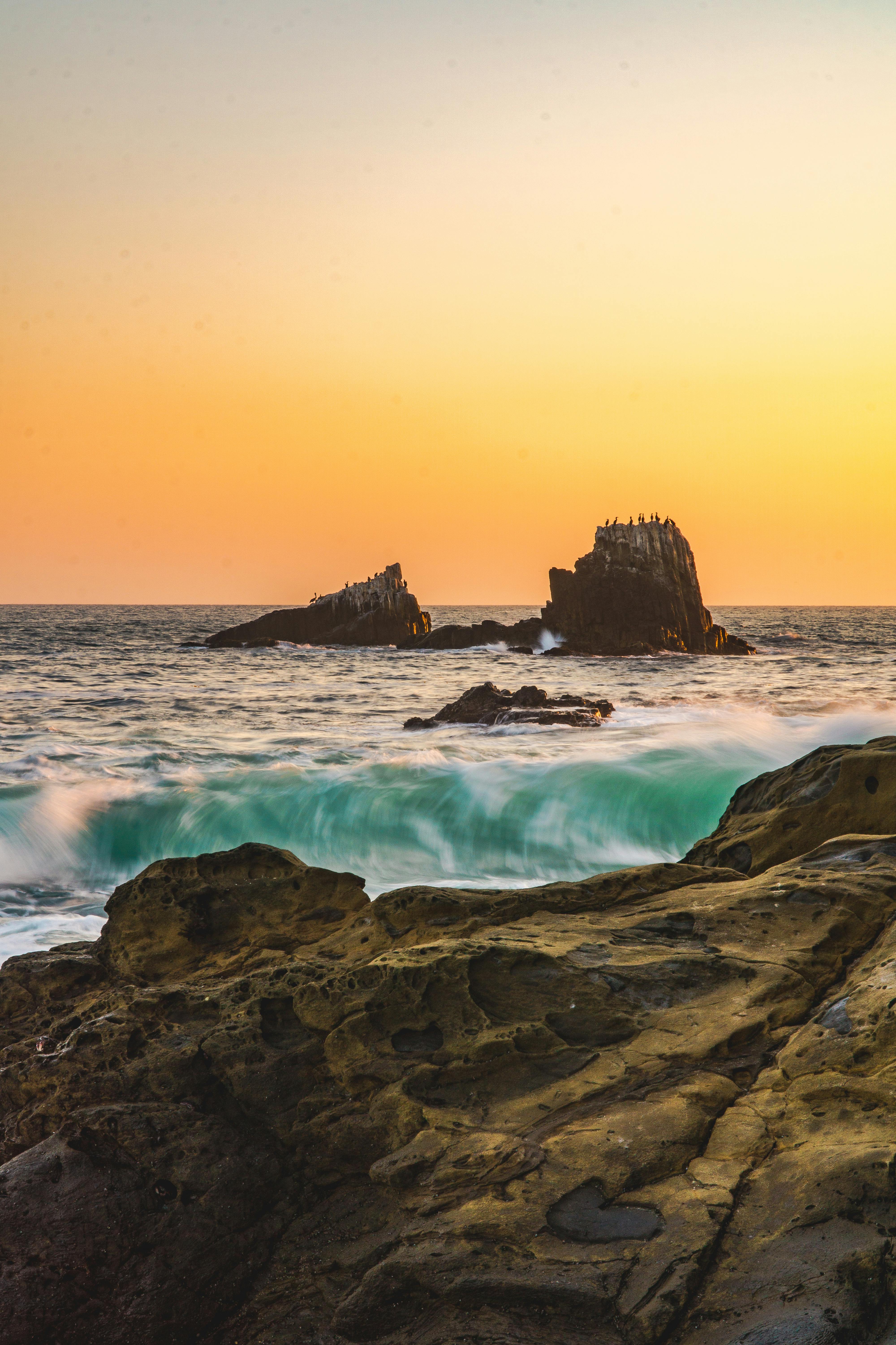 Stunning sunset view of ocean waves crashing against rugged rocks at Laguna Beach, California.