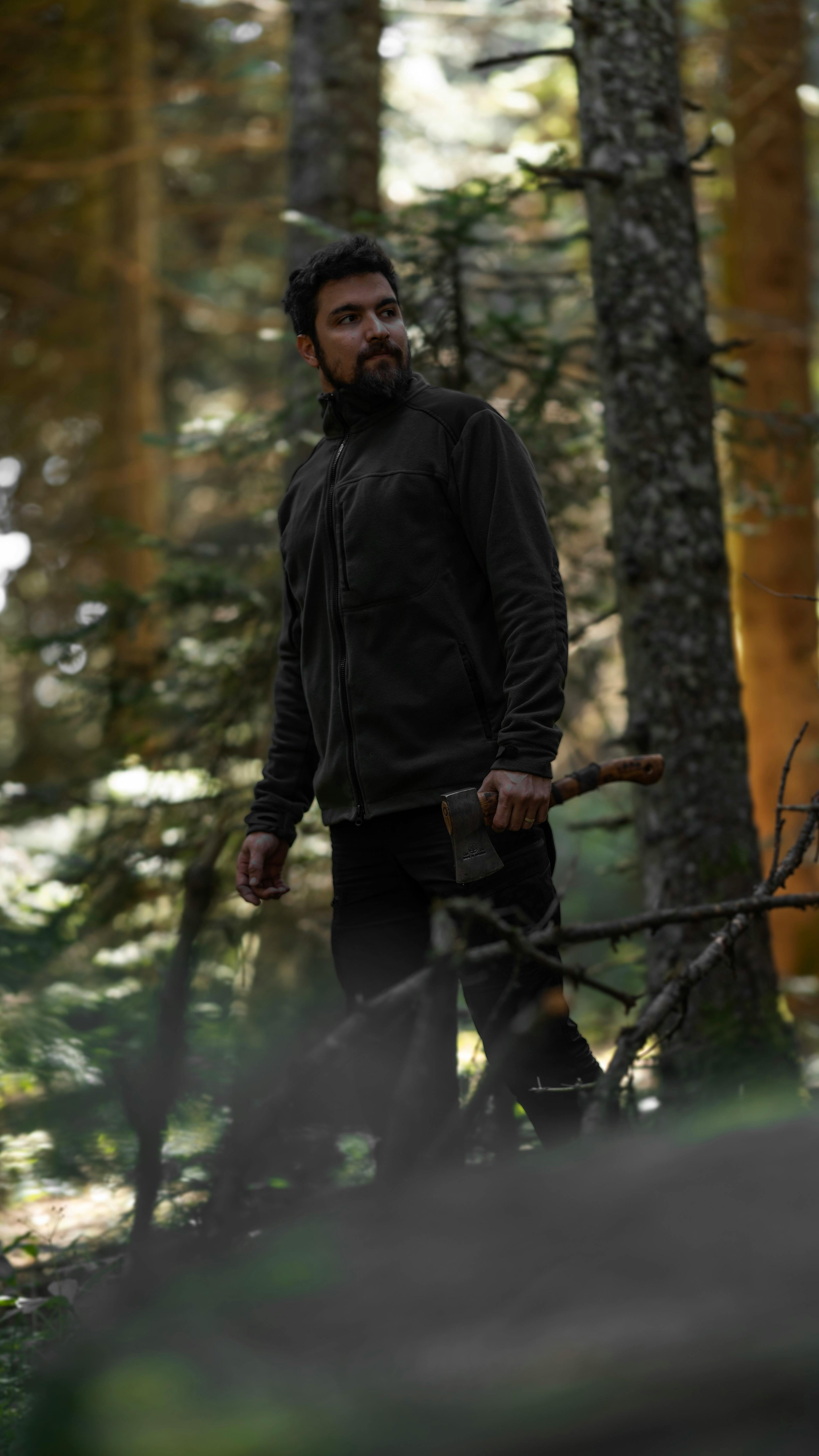 A bearded man holding an axe stands in a tranquil forest, showcasing bushcraft skills.