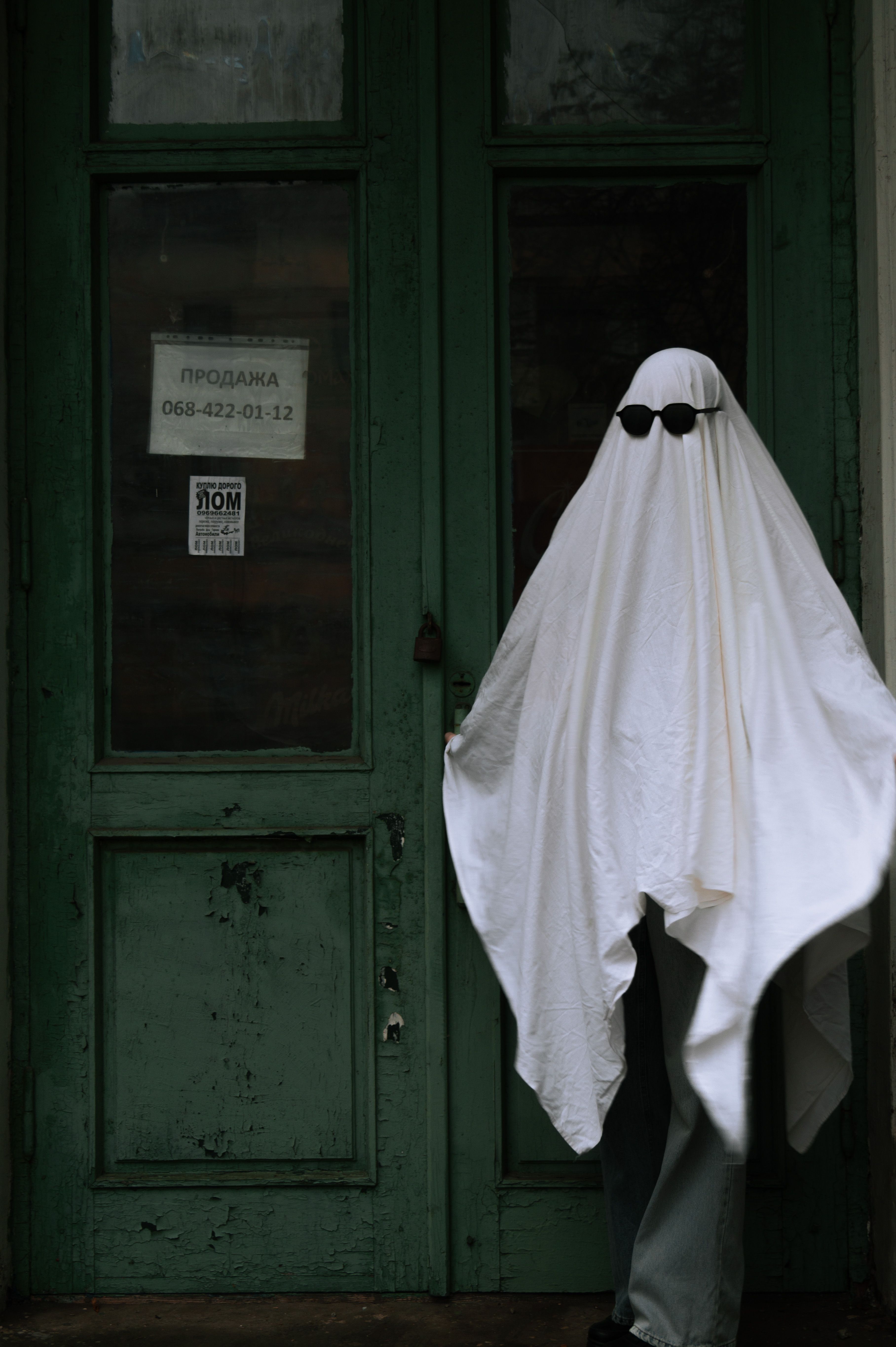 Spooky ghost figure in sunglasses stands in front of an old green door in Ukraine.