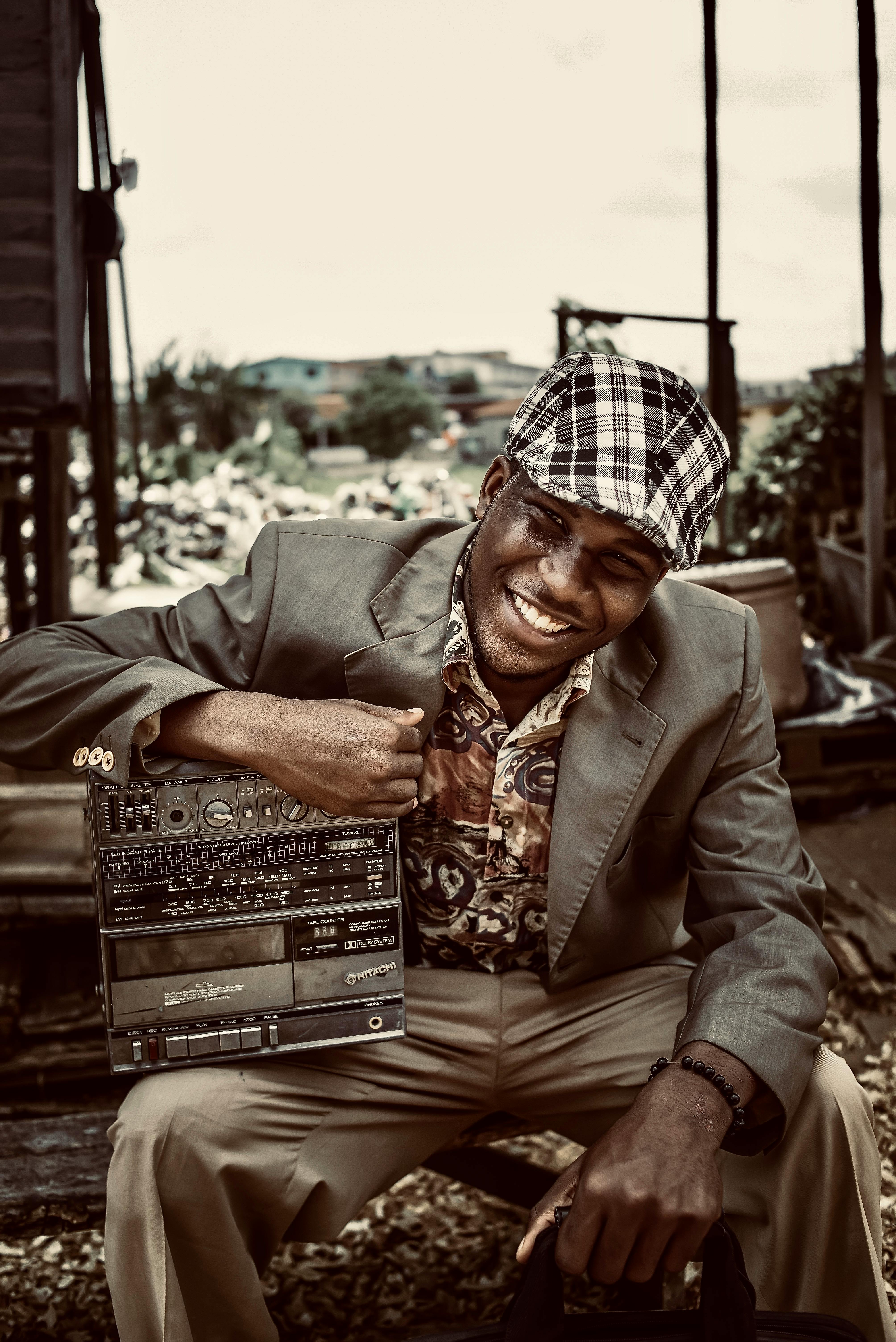 A joyful man in vintage fashion holding a retro radio, seated outdoors.