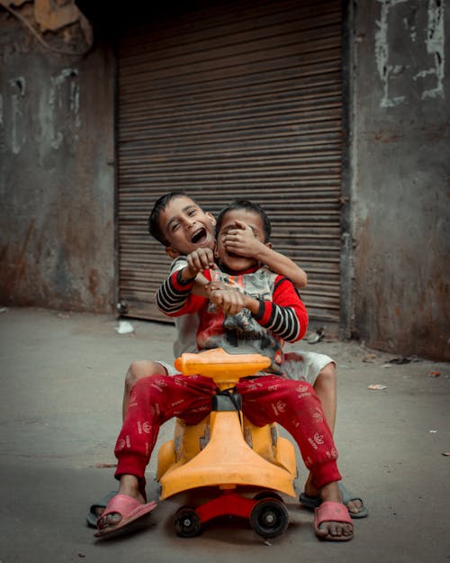 Two Little Brothers Playing on a Plastic Toy Car