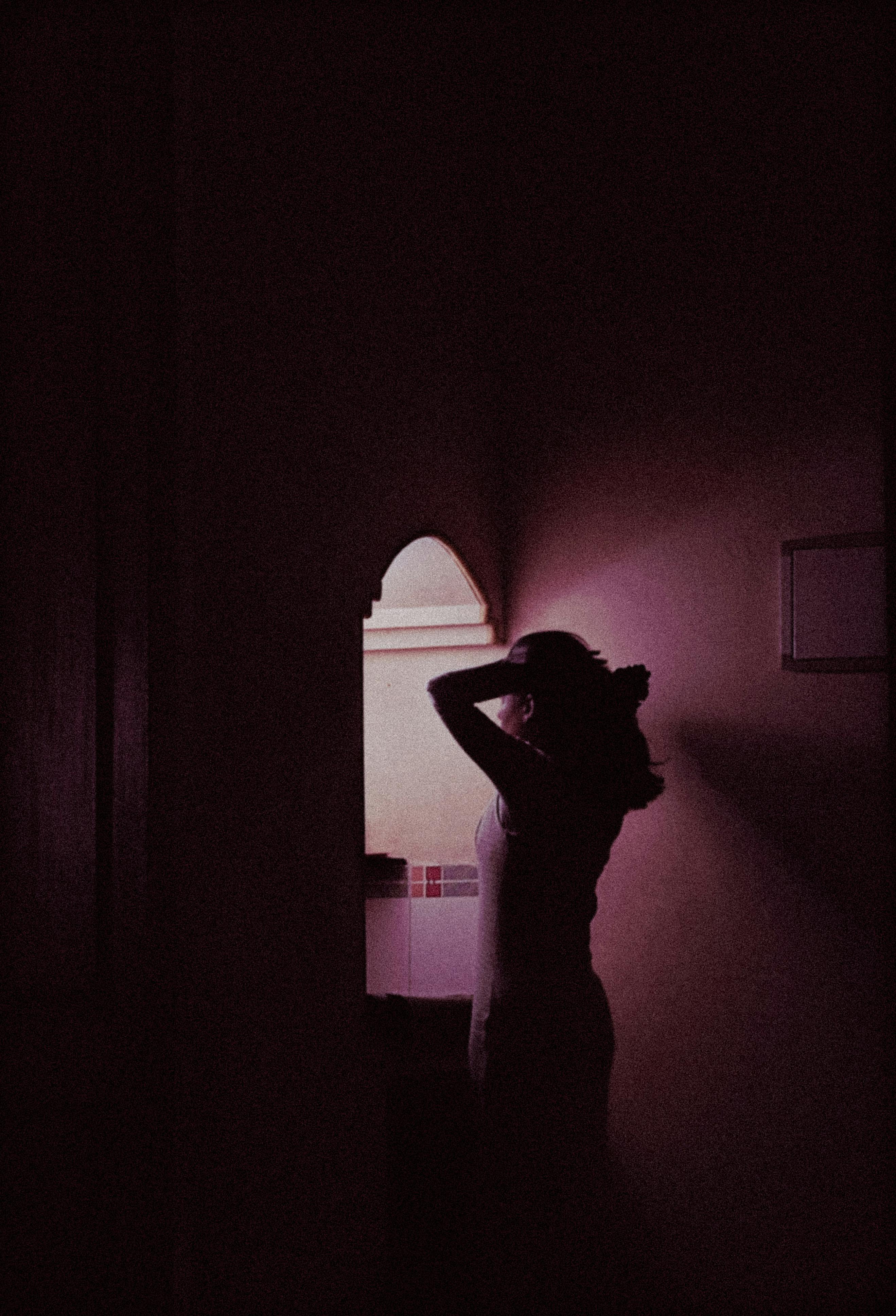 Silhouette of a woman standing near a window, creating a mysterious mood in a dimly lit room.