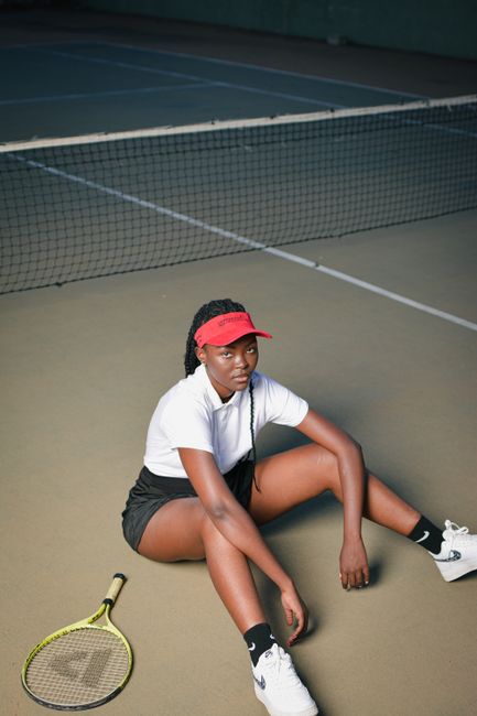 African woman in sportswear sits on tennis court, resting after match.