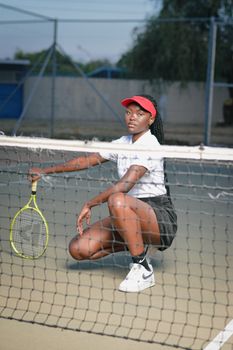 Focused female tennis player posing by the net on an outdoor court in Botswana.