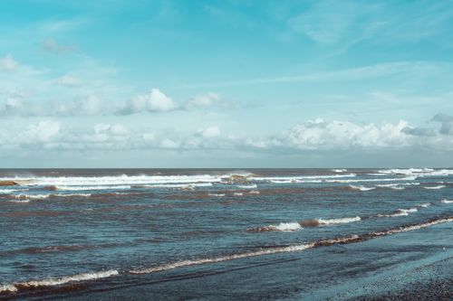 Free Serene seascape with gentle waves rolling under a vibrant blue sky and fluffy clouds. Stock Photo
