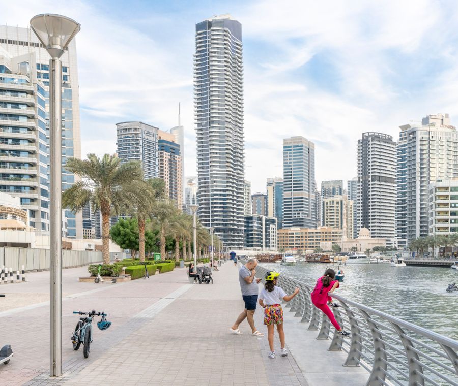A family enjoys a walk on the Dubai Marina promenade with skyline and water views.