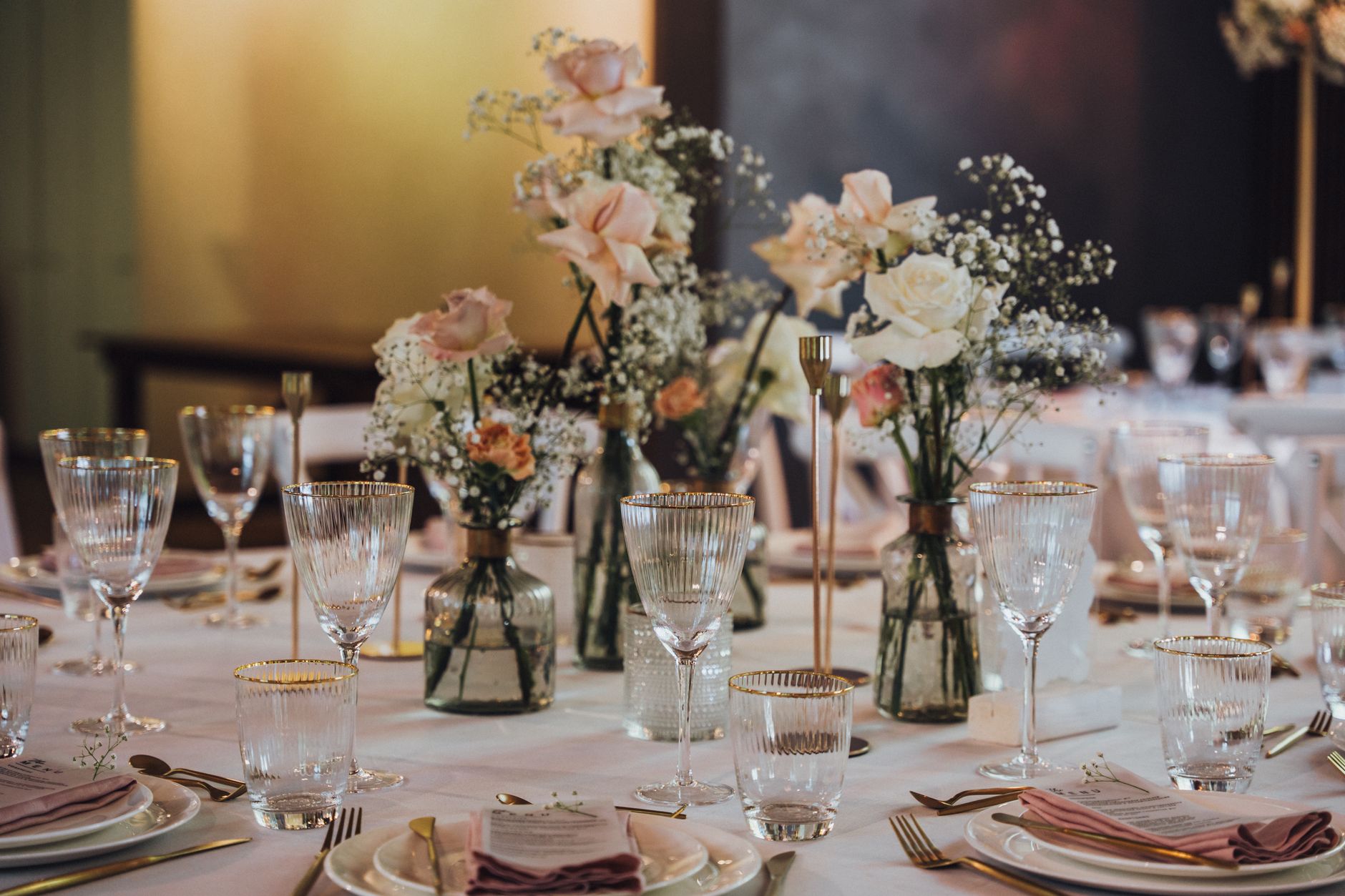 Beautifully arranged wedding table with elegant floral decorations and glassware in a soft-lit setting.