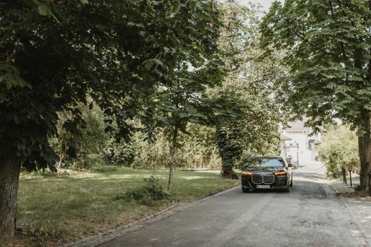 A sleek car driving down a tree-lined street in a serene summer setting.