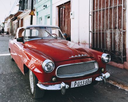A classic red convertible parked on a charming urban street with colorful buildings.