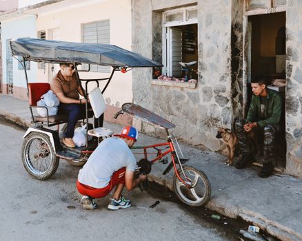 Men repairing a pedicab on a city street, showcasing urban life and transportation.