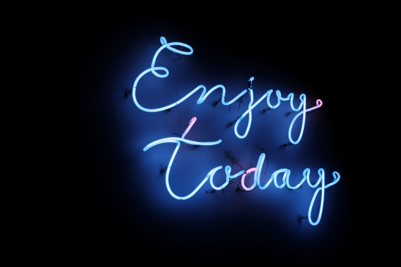 bright blue neon sign with the phrase enjoy today on a dark background