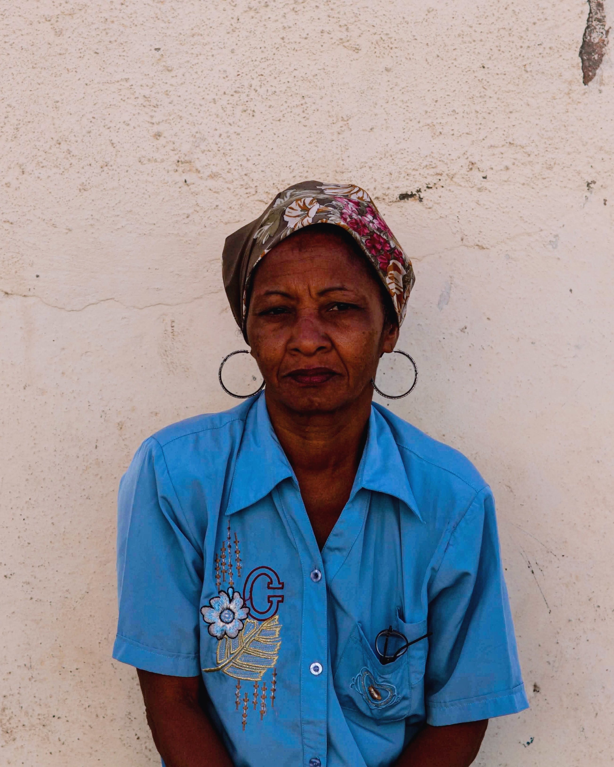 Portrait of an African woman with a headscarf and earrings against a textured wall.