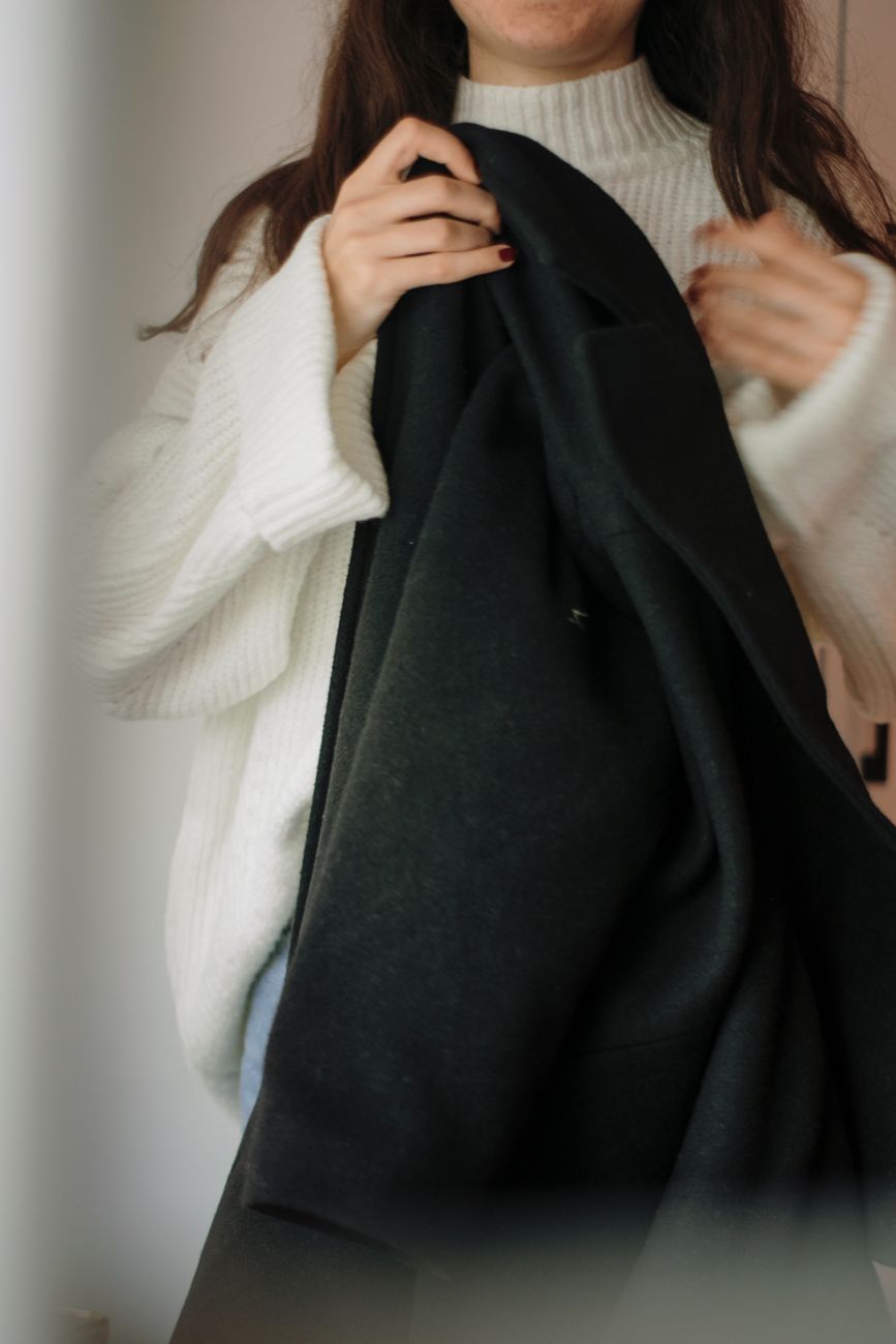 Stylish woman wearing a white sweater and holding a black coat indoors.
