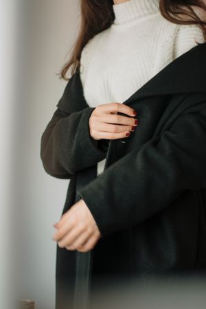 Woman adjusting a tailored black coat over a knit jumper, photo by Berna on Pexels