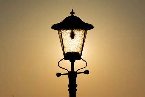 Free Silhouette of a vintage lamp post illuminated by the warm glow of a sunset. Stock Photo