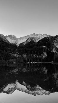 Captivating black and white reflection of mountains on Tovel Lake, Trentino, Italy, in winter.