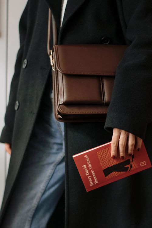 Free Stylish woman in coat holding a book and brown leather bag. Stock Photo