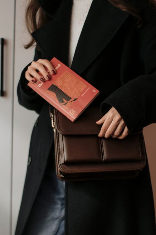 Free Stylish woman in a coat holding a brown leather bag and book. Stock Photo