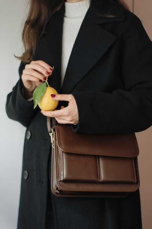 Free Elegant woman in a black coat holding a lemon and brown leather bag. Stock Photo