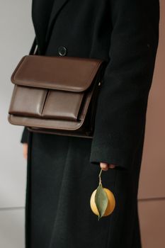 Stylish person holding a lemon with a brown leather bag, featuring elegant fashion in a vertical shot.