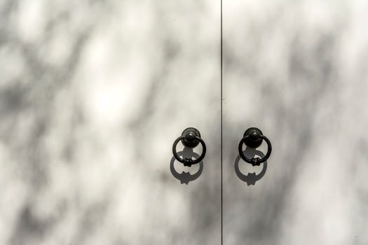 A minimalist image of dual door knockers casting shadows on a white surface, conveying an artistic feel.