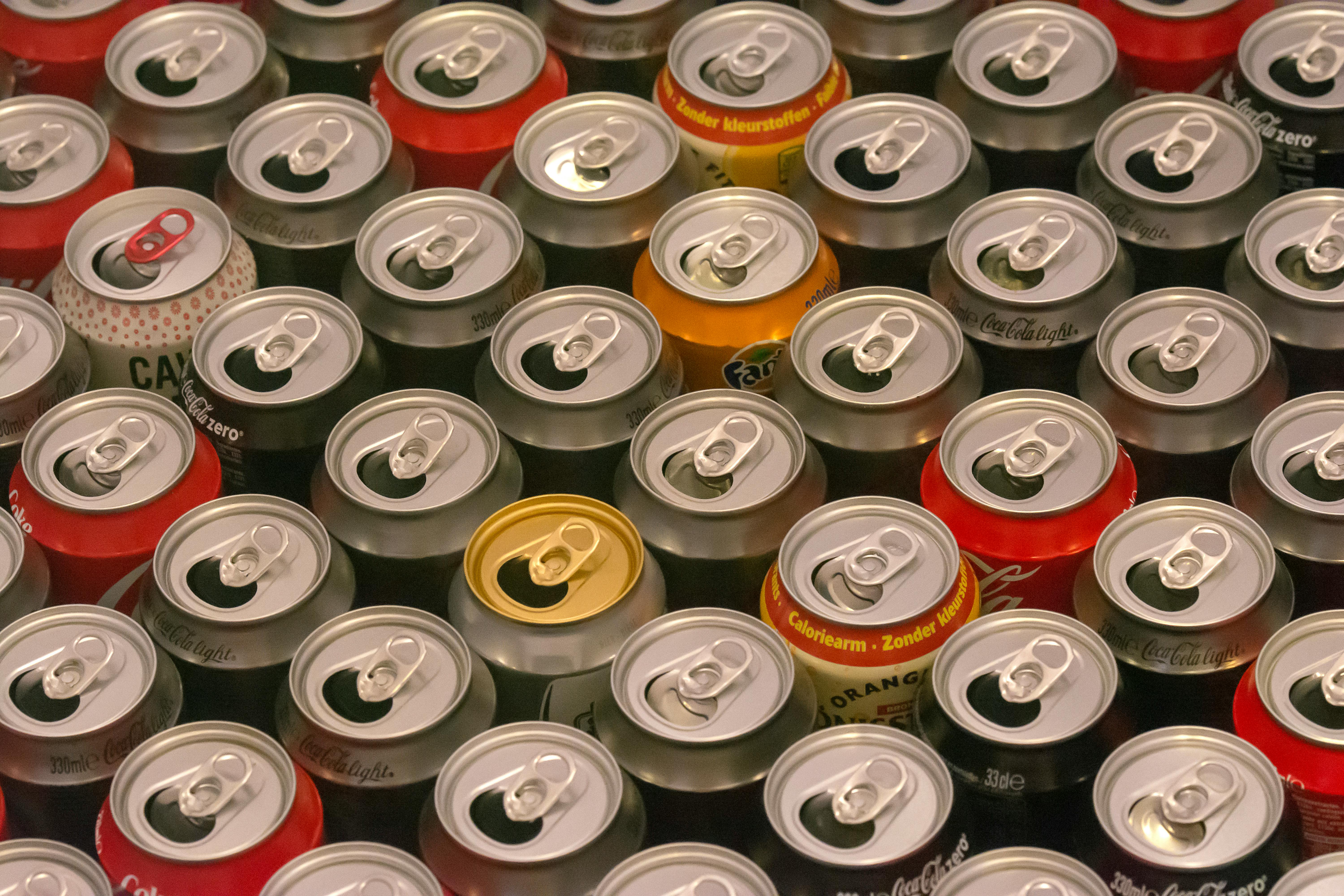Top view of various aluminum soda cans lined up in colorful rows, highlighting recycle potential.