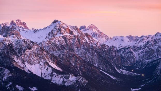 Breathtaking view of the snow-capped Dolomites at sunset with a serene orange sky.