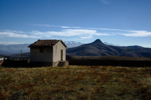 Free An isolated hut stands in a vast mountainous landscape under a clear blue sky. Stock Photo