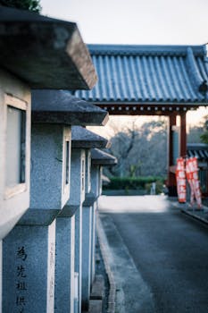 Series of stone lanterns lining a temple pathway with traditional Japanese architecture in the background.