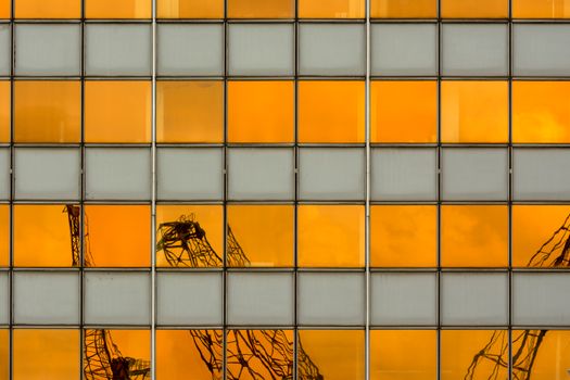 Cranes reflected in glass building windows with a striking orange hue.