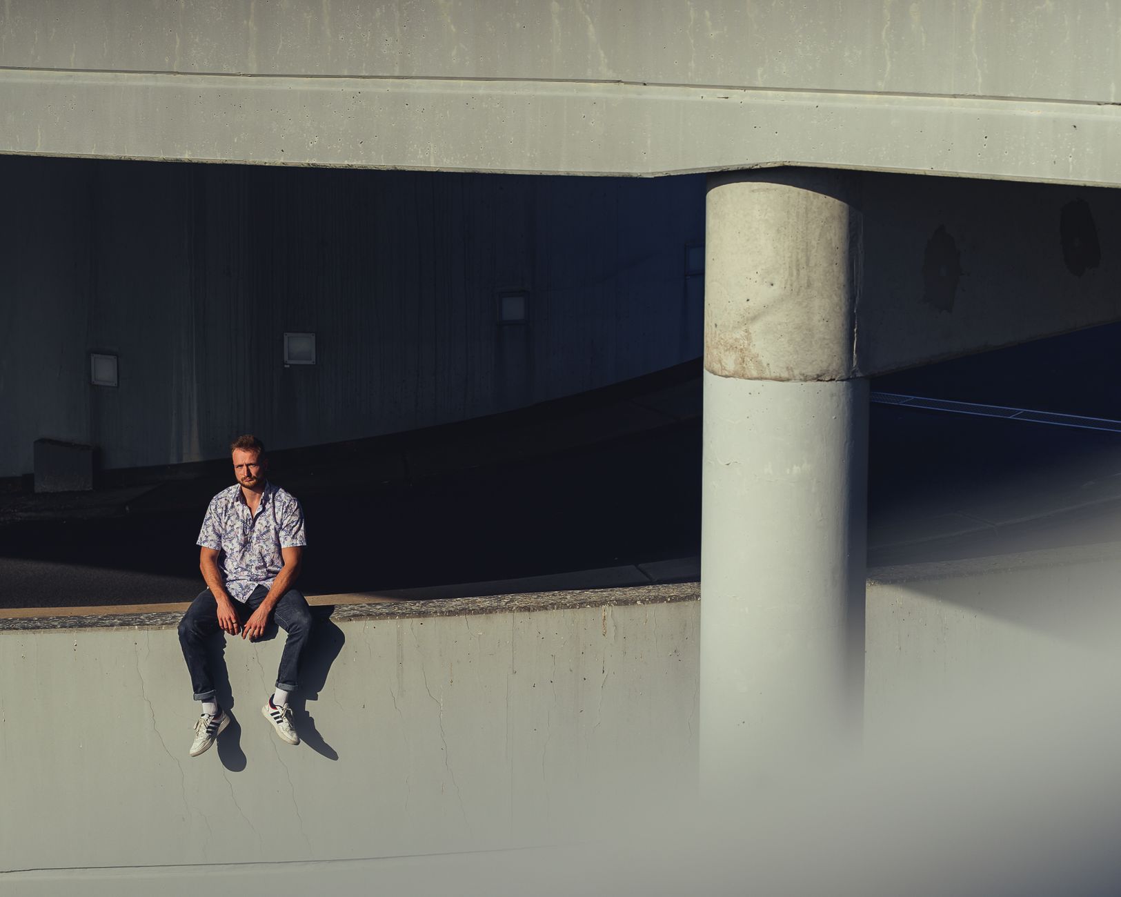 A man sitting on an urban concrete ledge captured in a moody fashion setting.