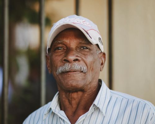 Free Warm portrait of a smiling senior man with a mustache wearing a striped shirt and baseball cap. Stock Photo