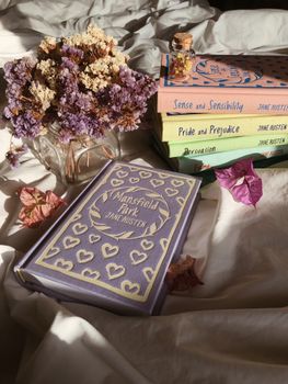 Elegant scene with Jane Austen books and dried flowers on white sheets.
