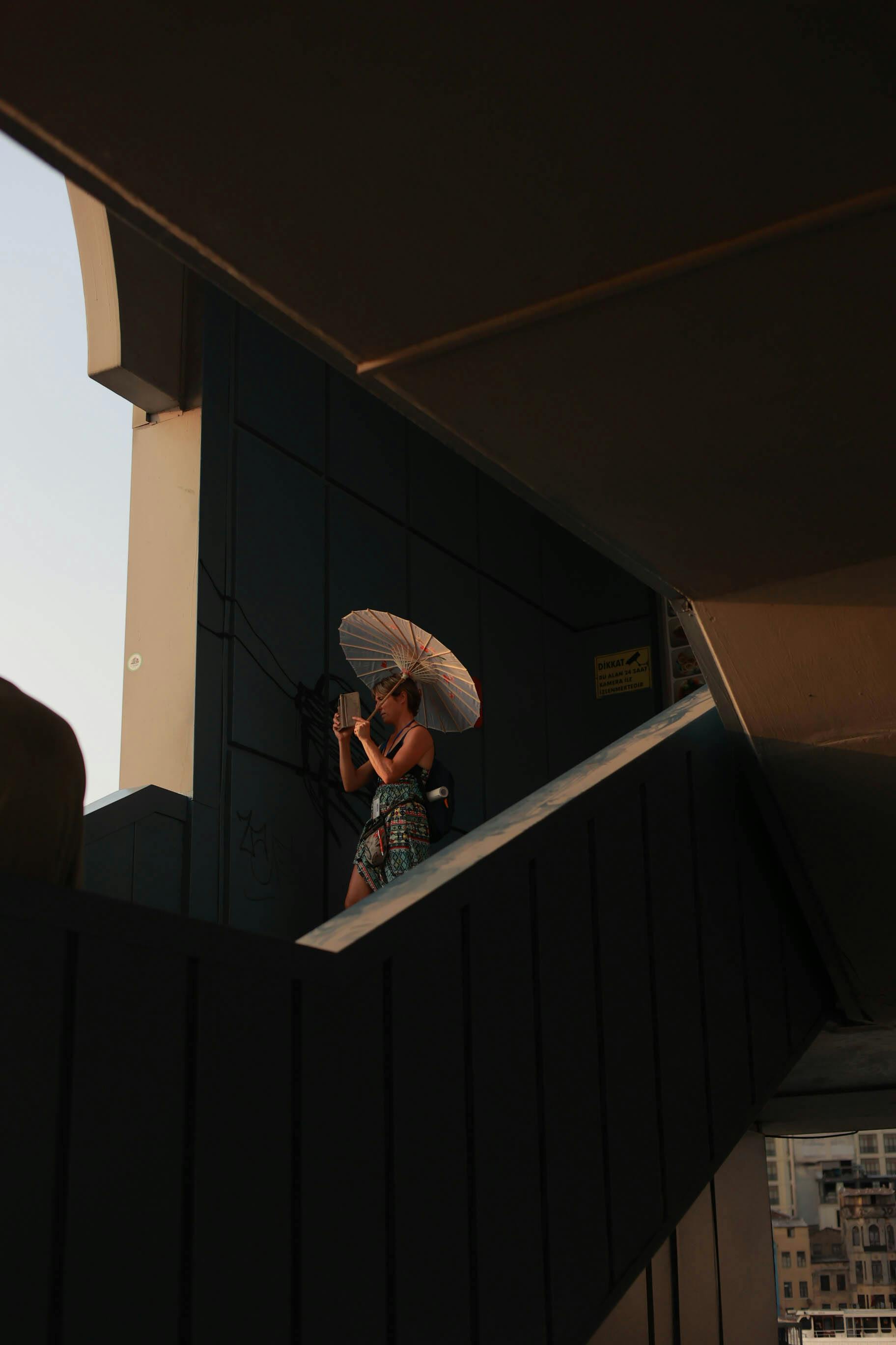 A woman holding an umbrella walks up modern stairs with geometric architecture.