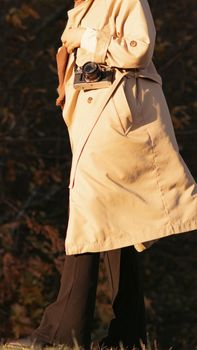 Fashionable woman in autumn coat holding a vintage camera outdoors in fall setting.