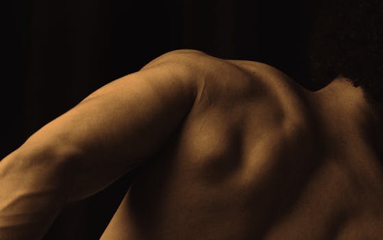 Artistic close-up of a muscular man's back and shoulder with dramatic lighting.