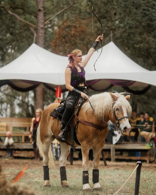 Woman in Fantasy Costume Holding up Bow while Riding Horseback