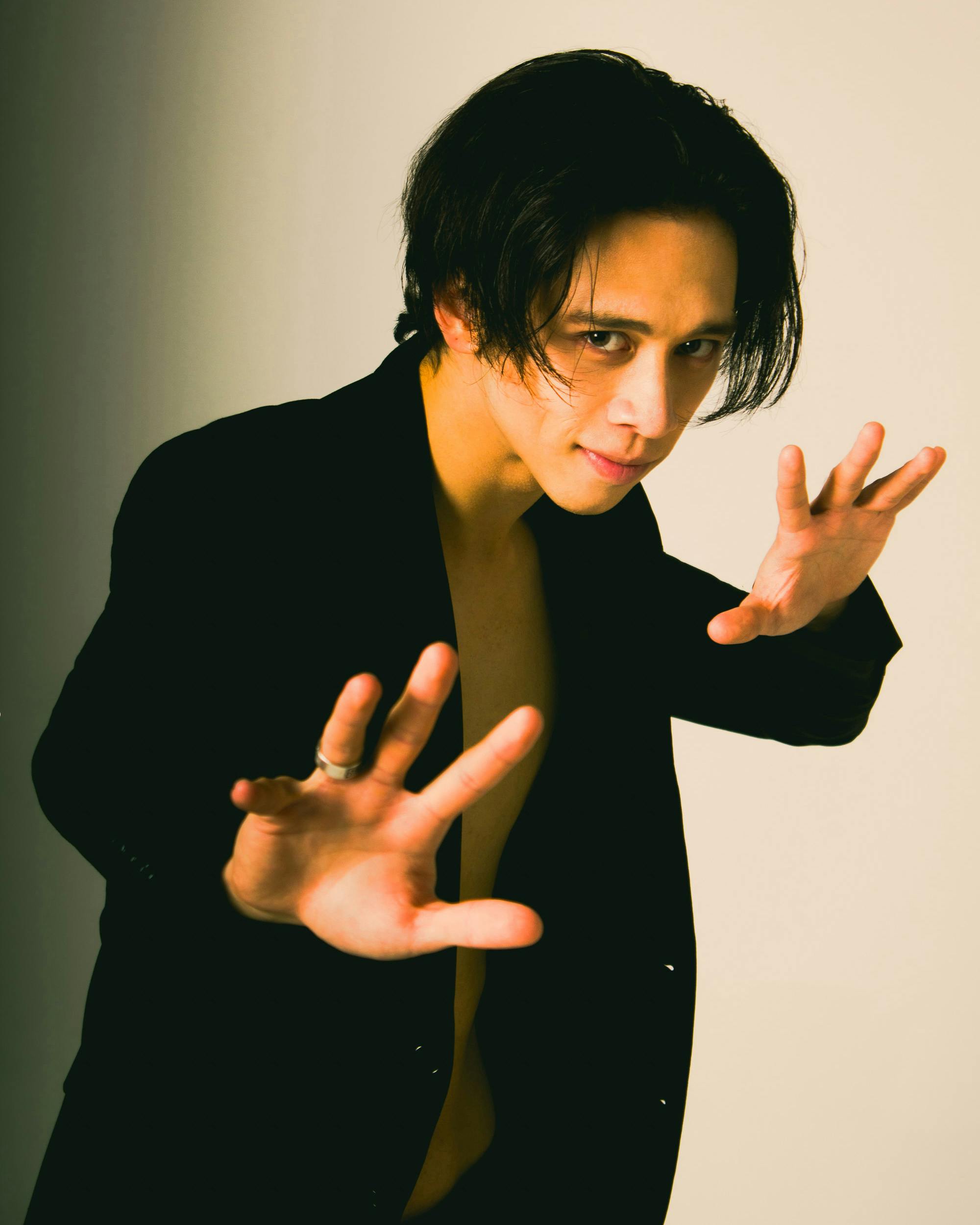 A creative studio portrait of a male model posing with dramatic hands in a stylish black suit.