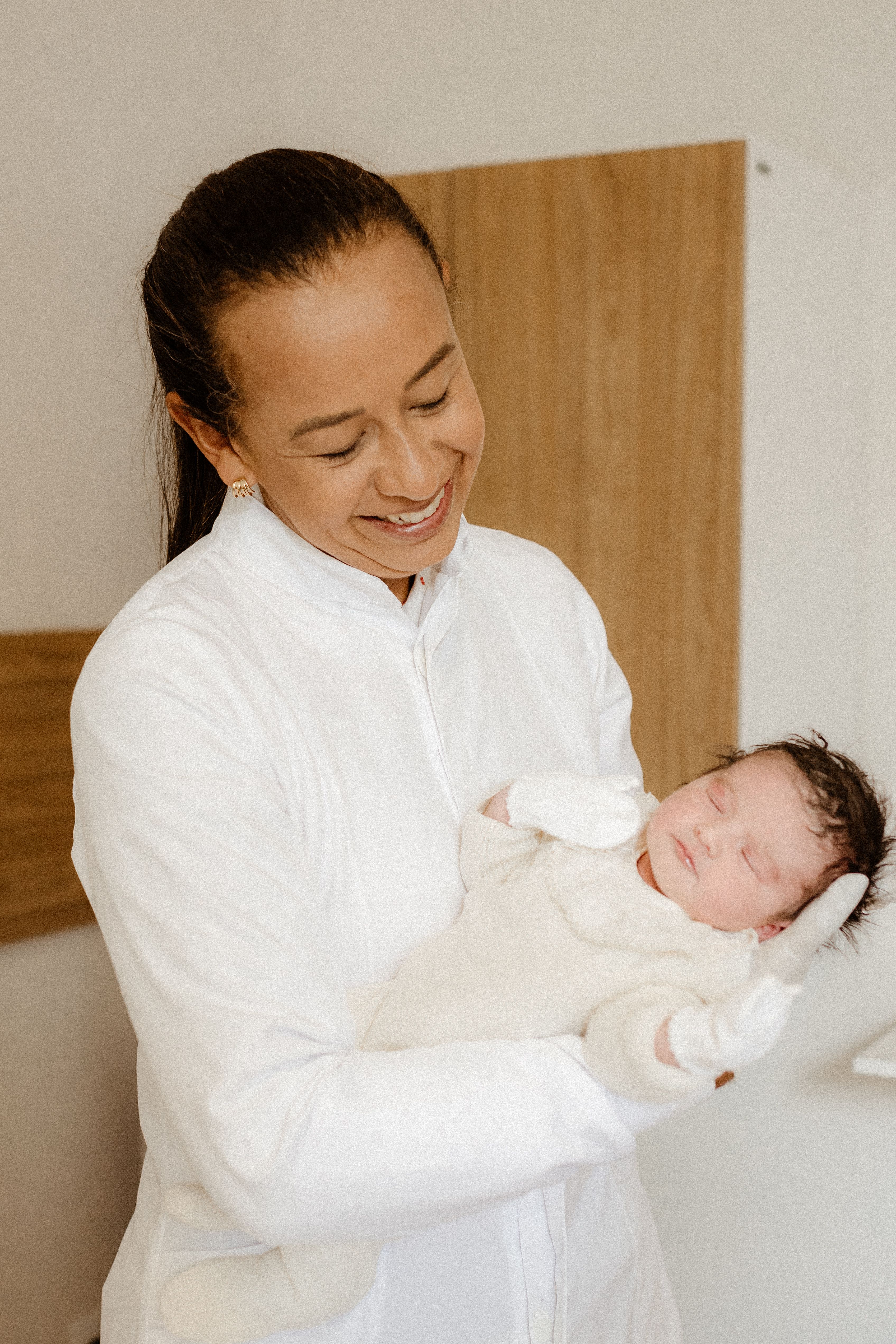Smiling doctor gently holding a sleeping newborn in a hospital environment.
