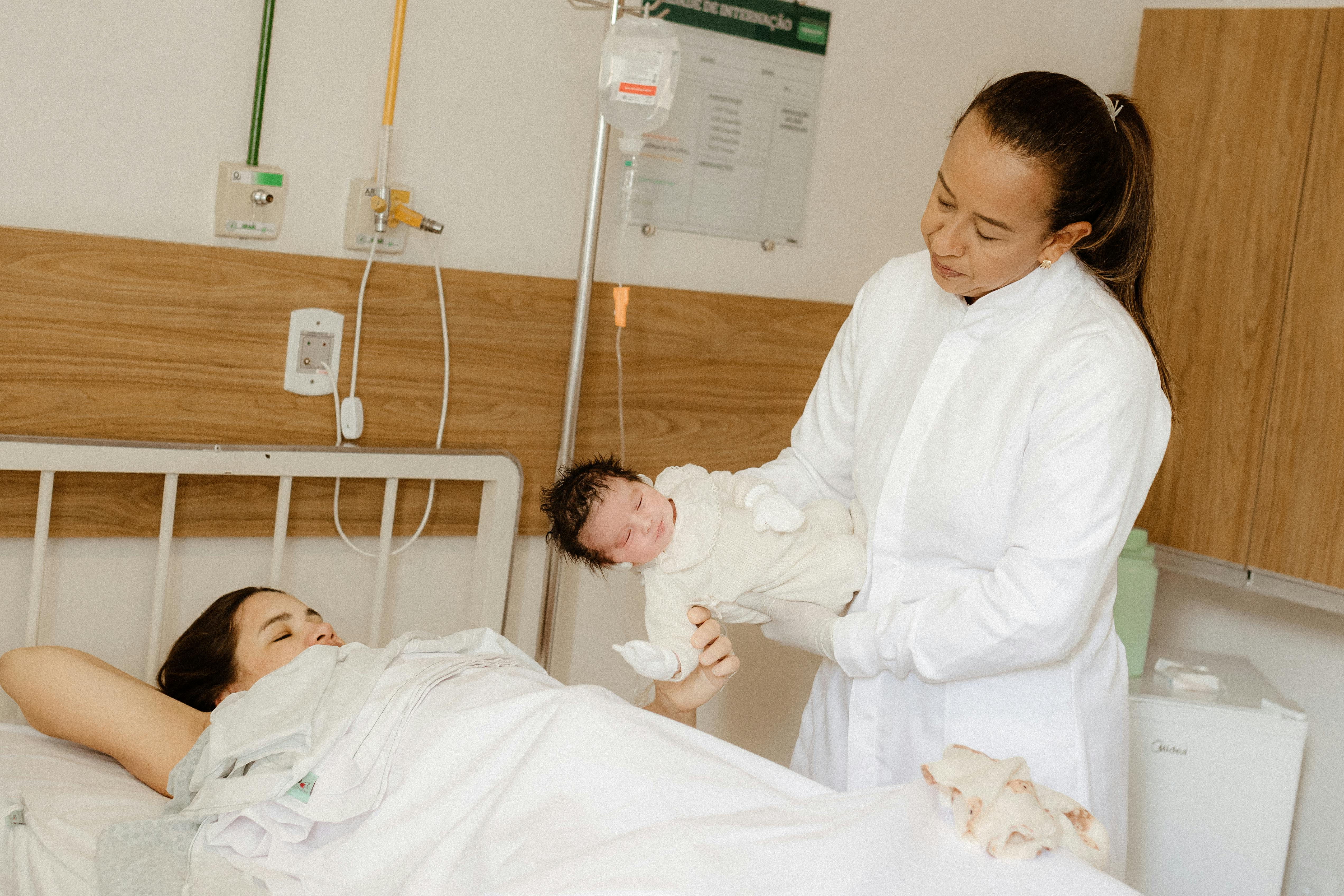 a woman in a white coat holding a baby in a hospital bed