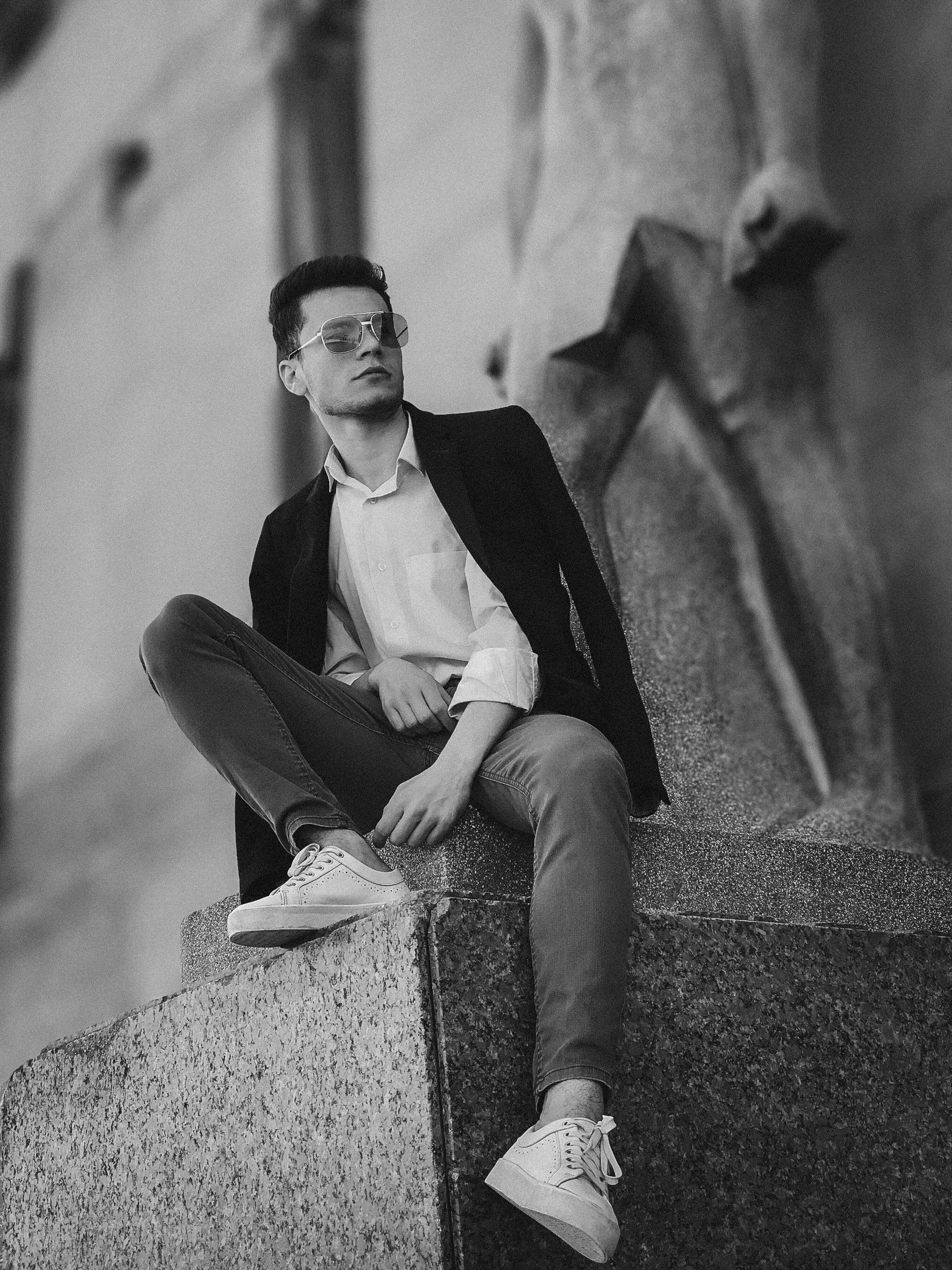Grayscale Photography of Man Sitting Beside Statue