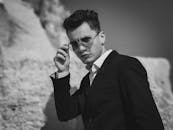 岩石景观中，一个戴着墨镜、穿着西装的男人黑白肖像