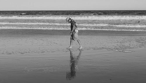 Black and White Photo of Man Walking across Beach