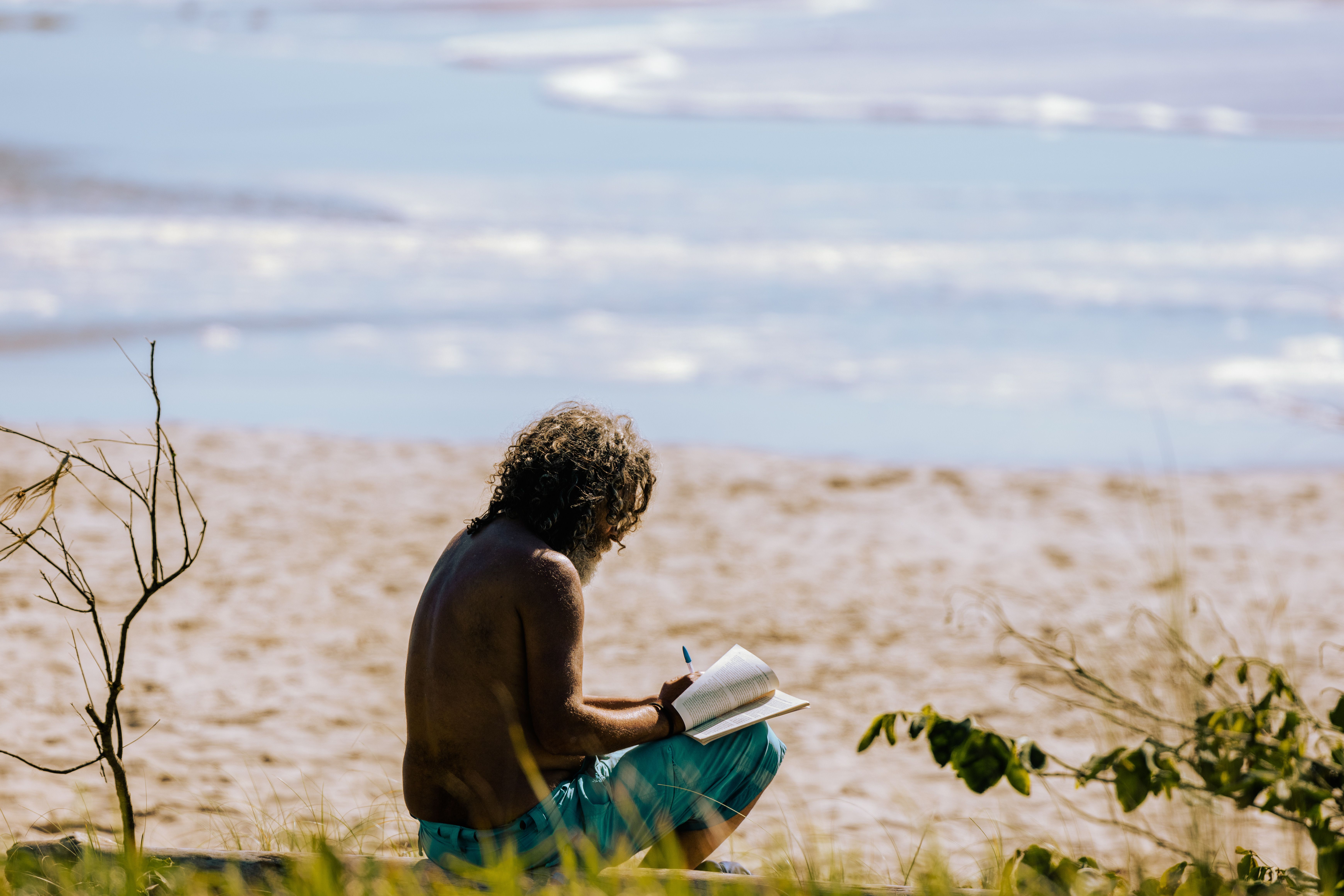 A man enjoying a quiet moment near the sea, writing in a notebook on a sunny beach.