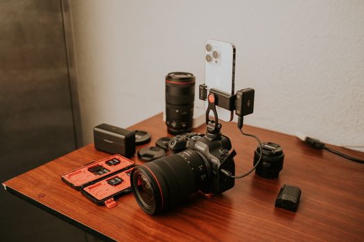 Close-up of professional camera gear including a DSLR and smartphone on a wooden table.